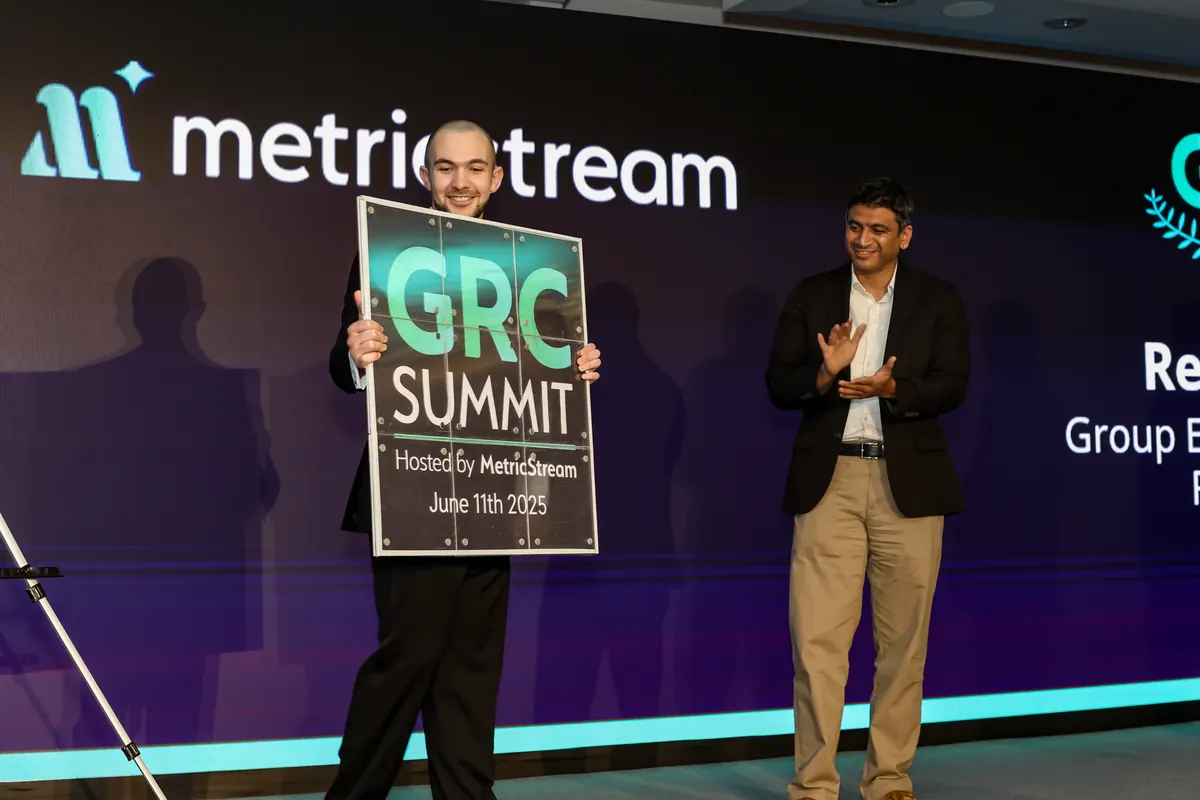 Daniel Bower on stage holding a custom GRC Summit sign, hosted by MetricStream, 11 June 2025