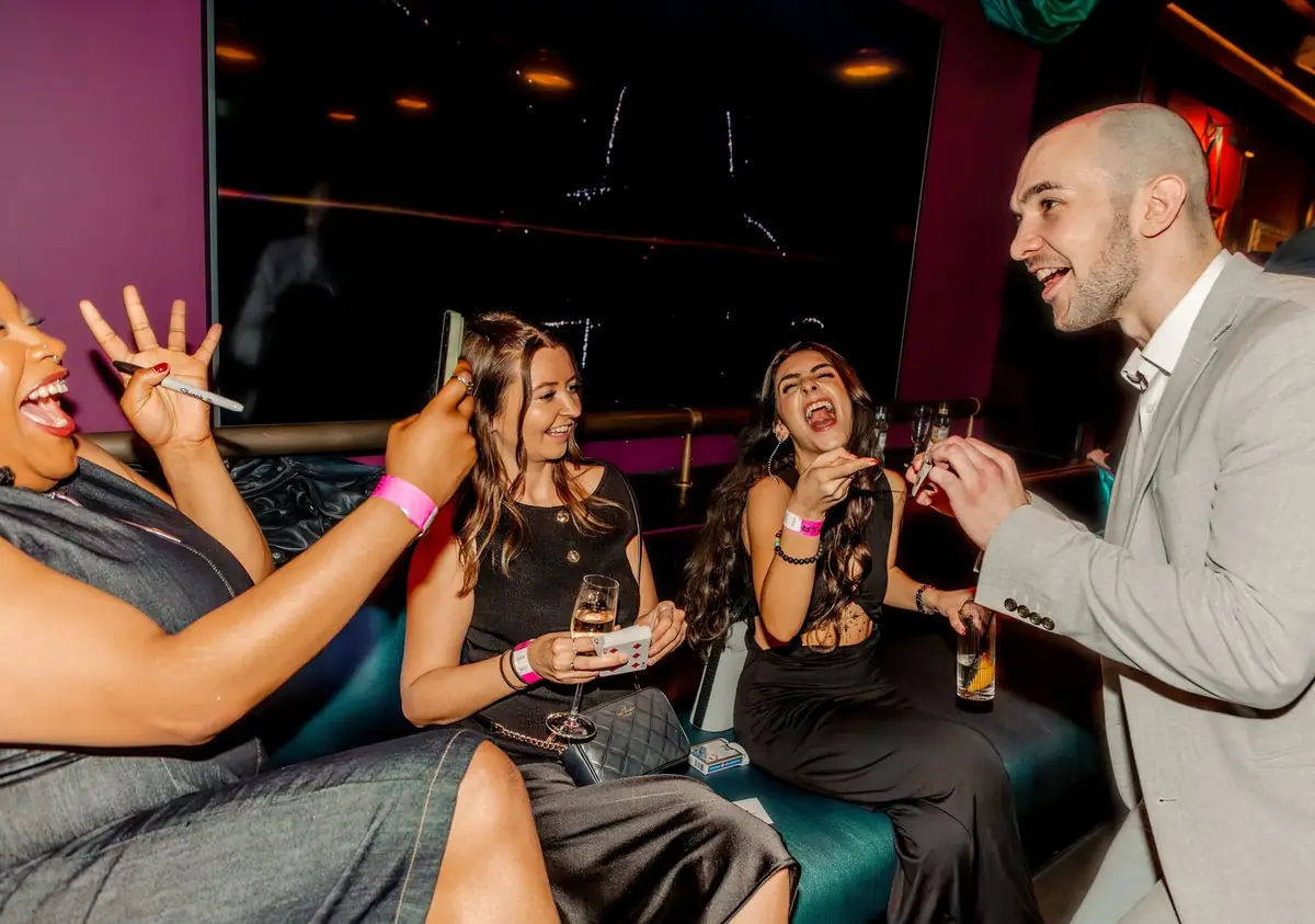 Guests smiling and reacting as magician performs close-up illusions at corporate party.