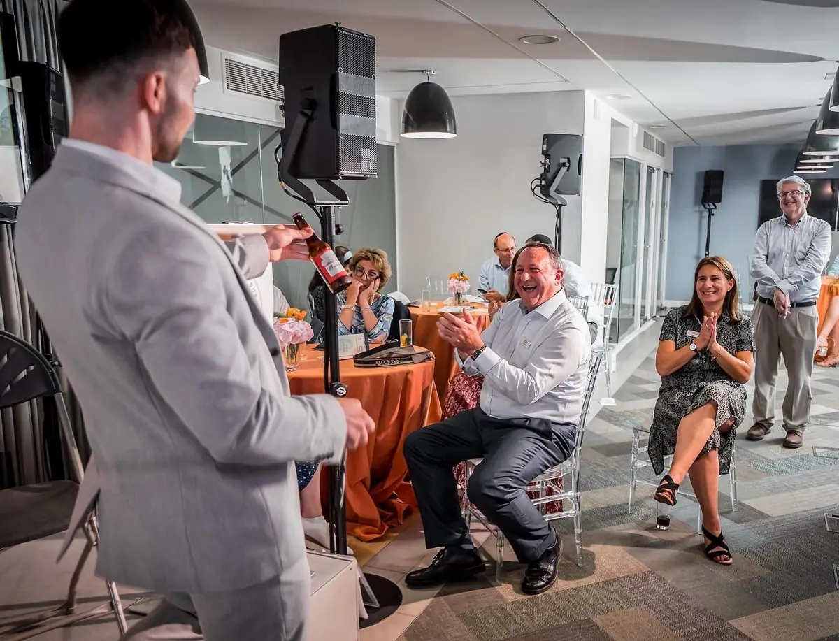 Magician giving a magic treat as guests smile and applaud at reception tables.