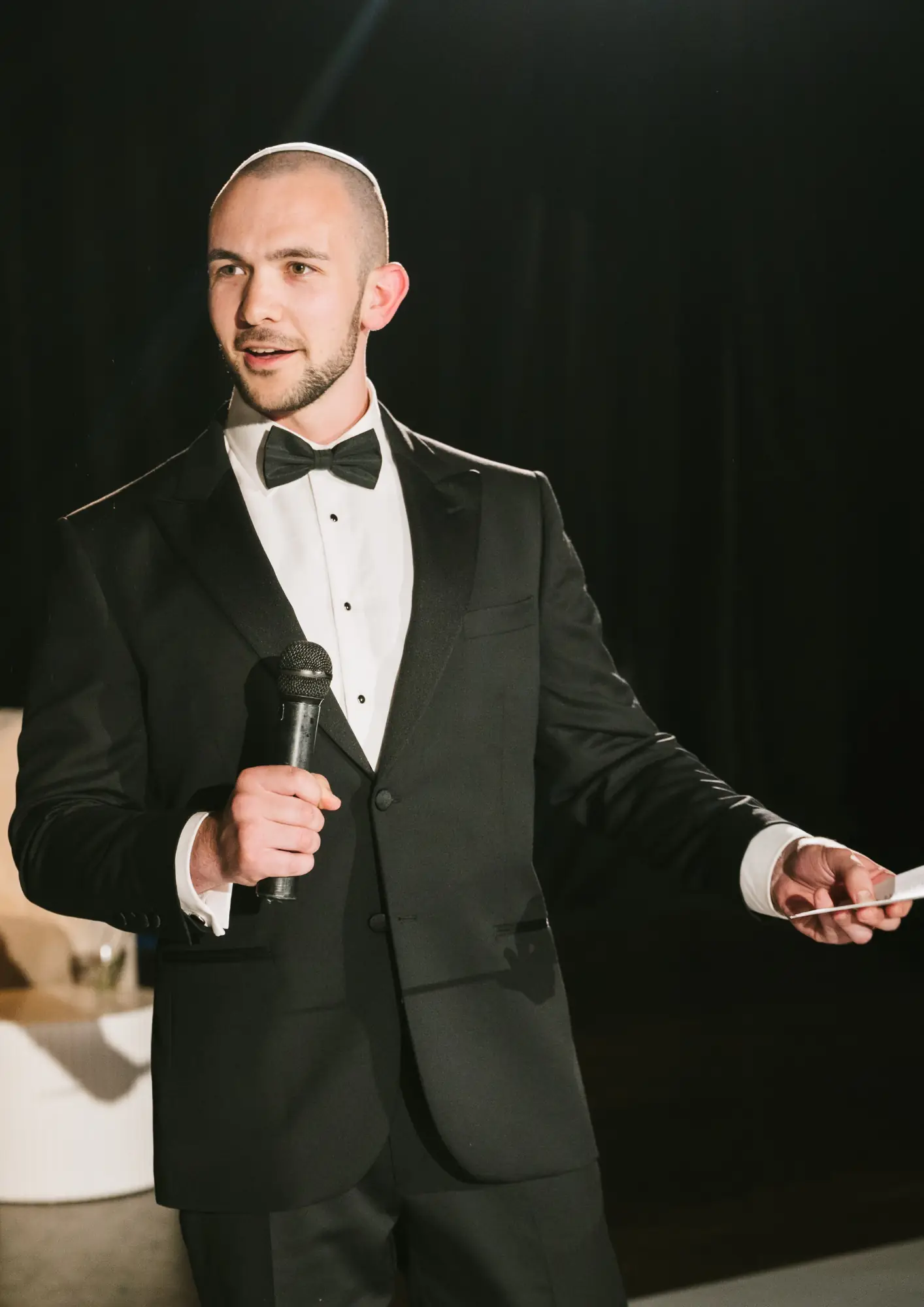 Daniel Bower wearing a kippah and black tie, holding a microphone